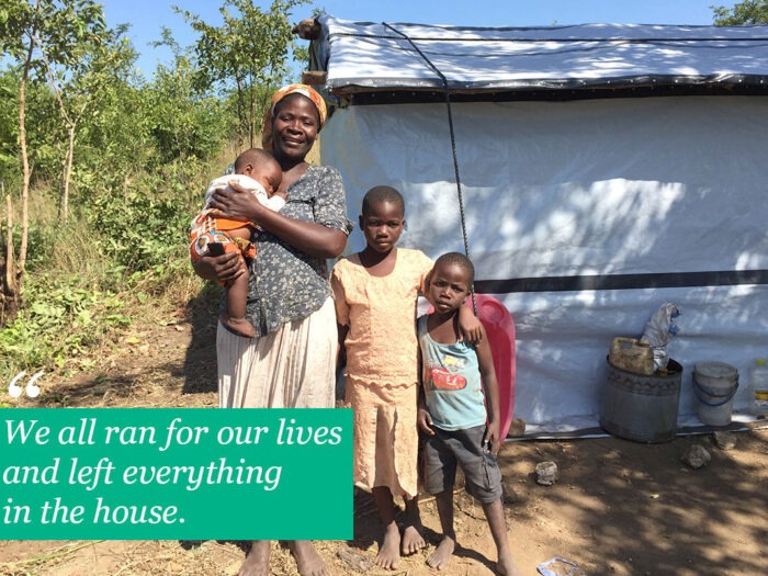 Woman standing with children outside home with tarpaulin walls in Malawi
