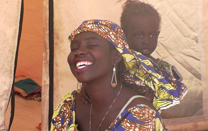 Woman smiling a camera with a baby in a carrier on her back