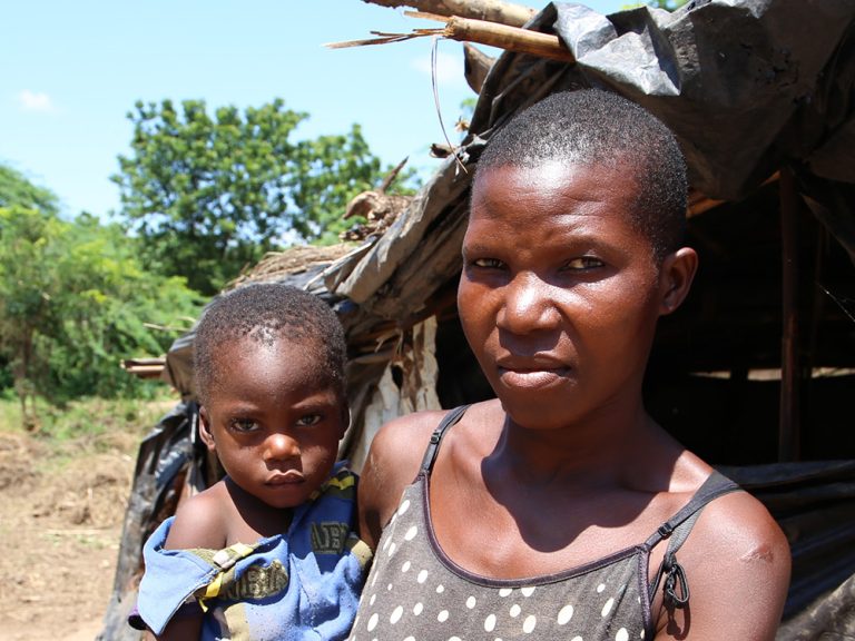 Woman holding a child outside a temporary structure in Malawi