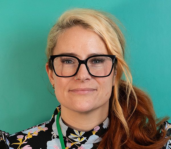 Woman wearing glasses with blonde and brown hair against a green backdrop